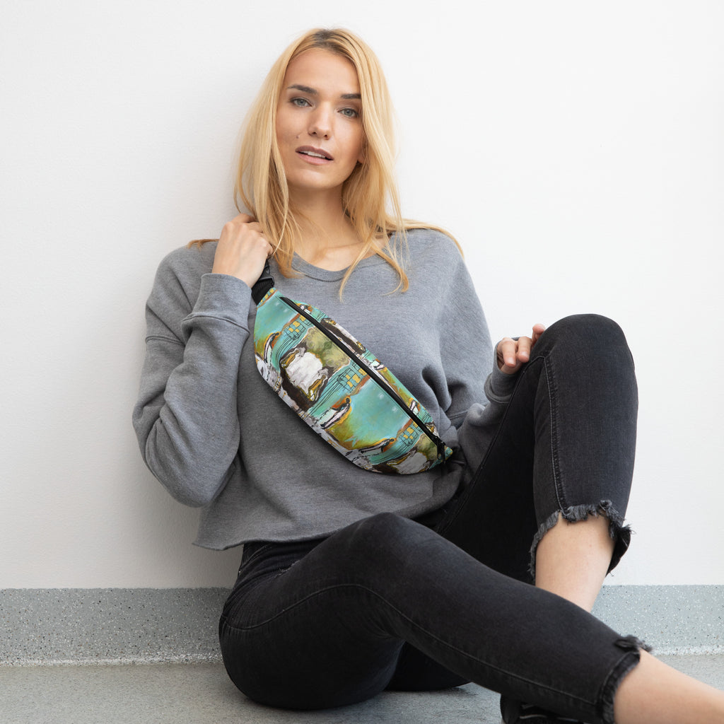 Woman in a gray sweatshirt and black jeans sitting by a wall, the fanny pack worn crossbody