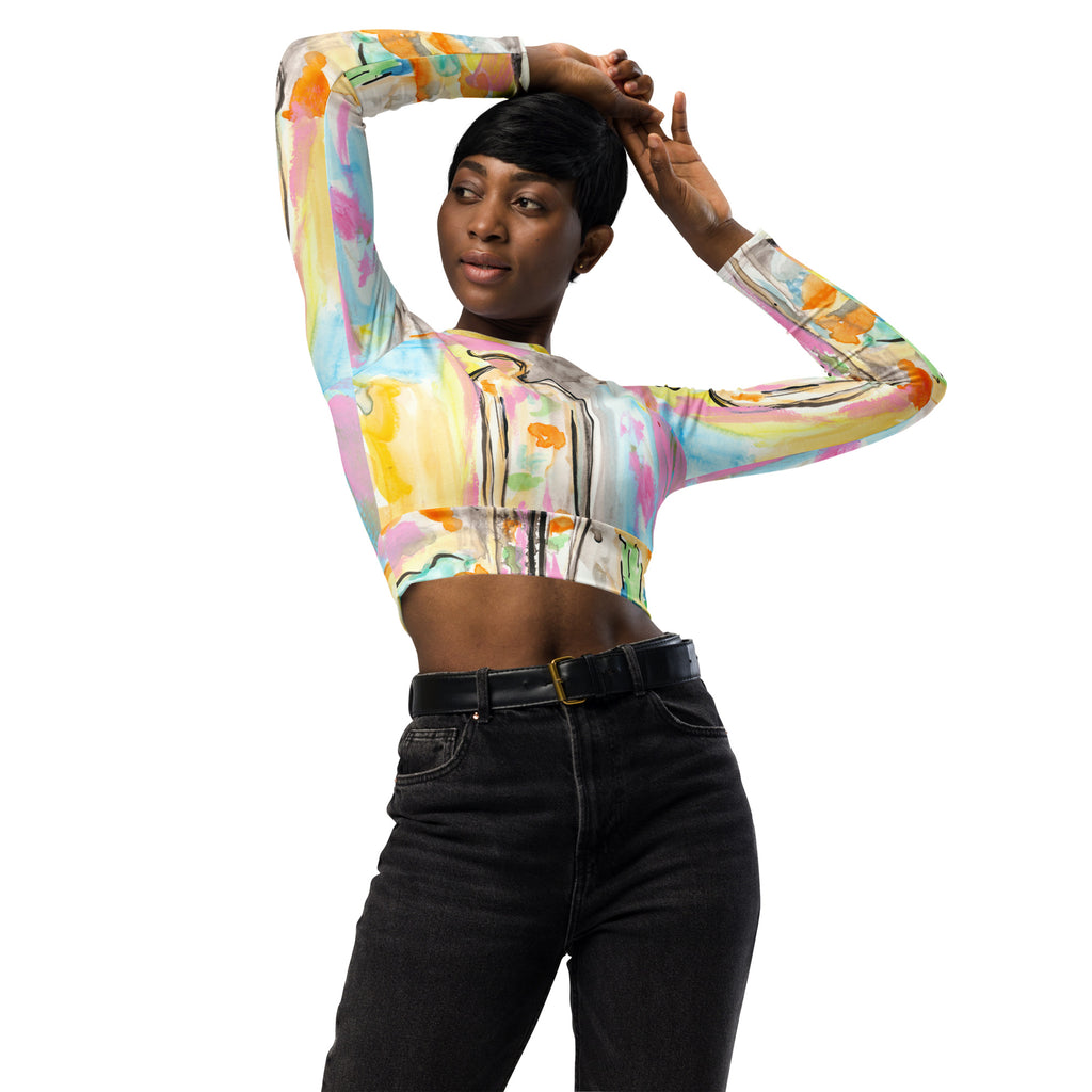 Model with arms raised over her head in the pastel crop top, black jeans and belt