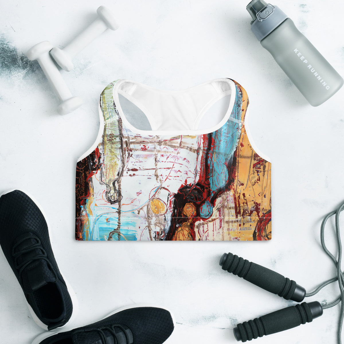 Front of the sports bra laid flat near dumbbells, a water bottle, sneakers and jump rope