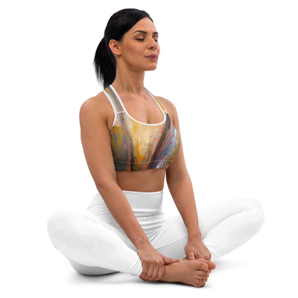 Seated model with eyes closed holding her feet, front of the gold bra visible