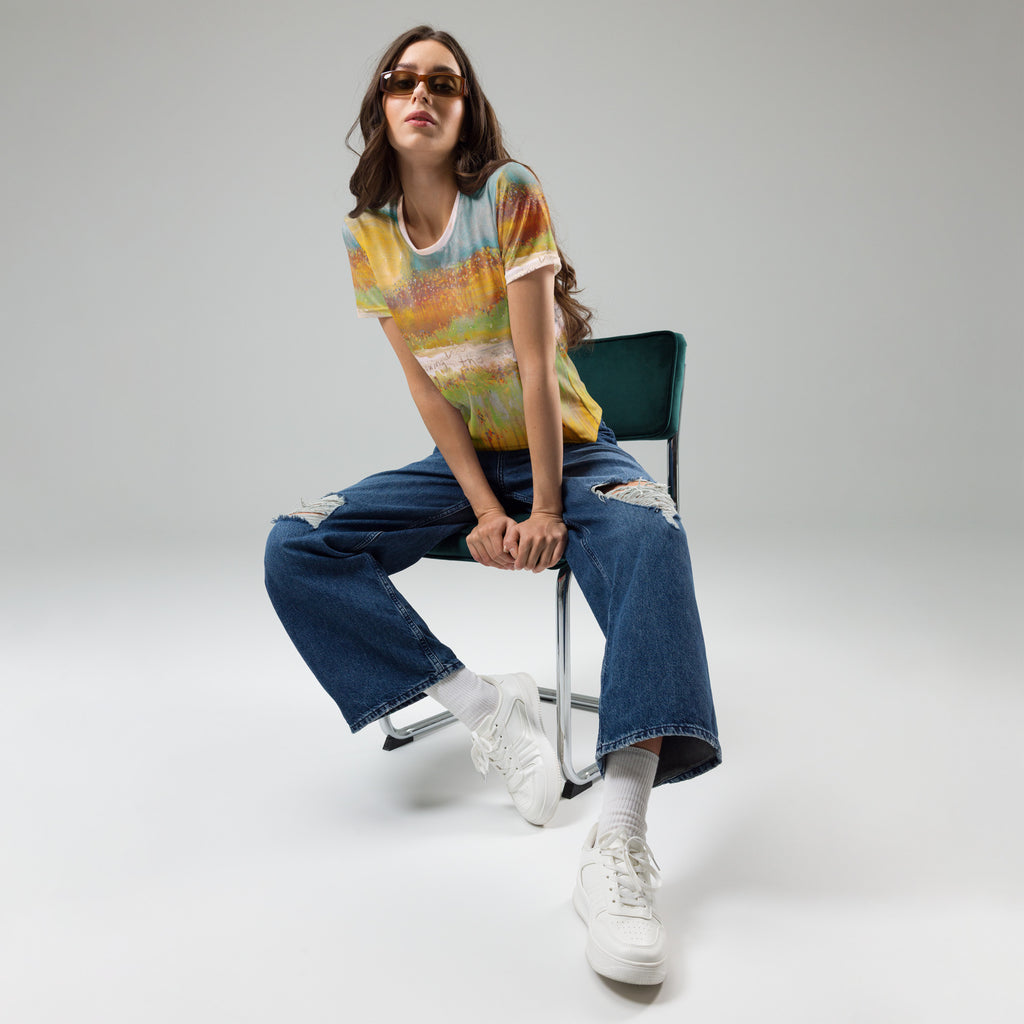 Model in sunglasses seated on a green chair in the painted tee, wide ripped jeans and white sneakers